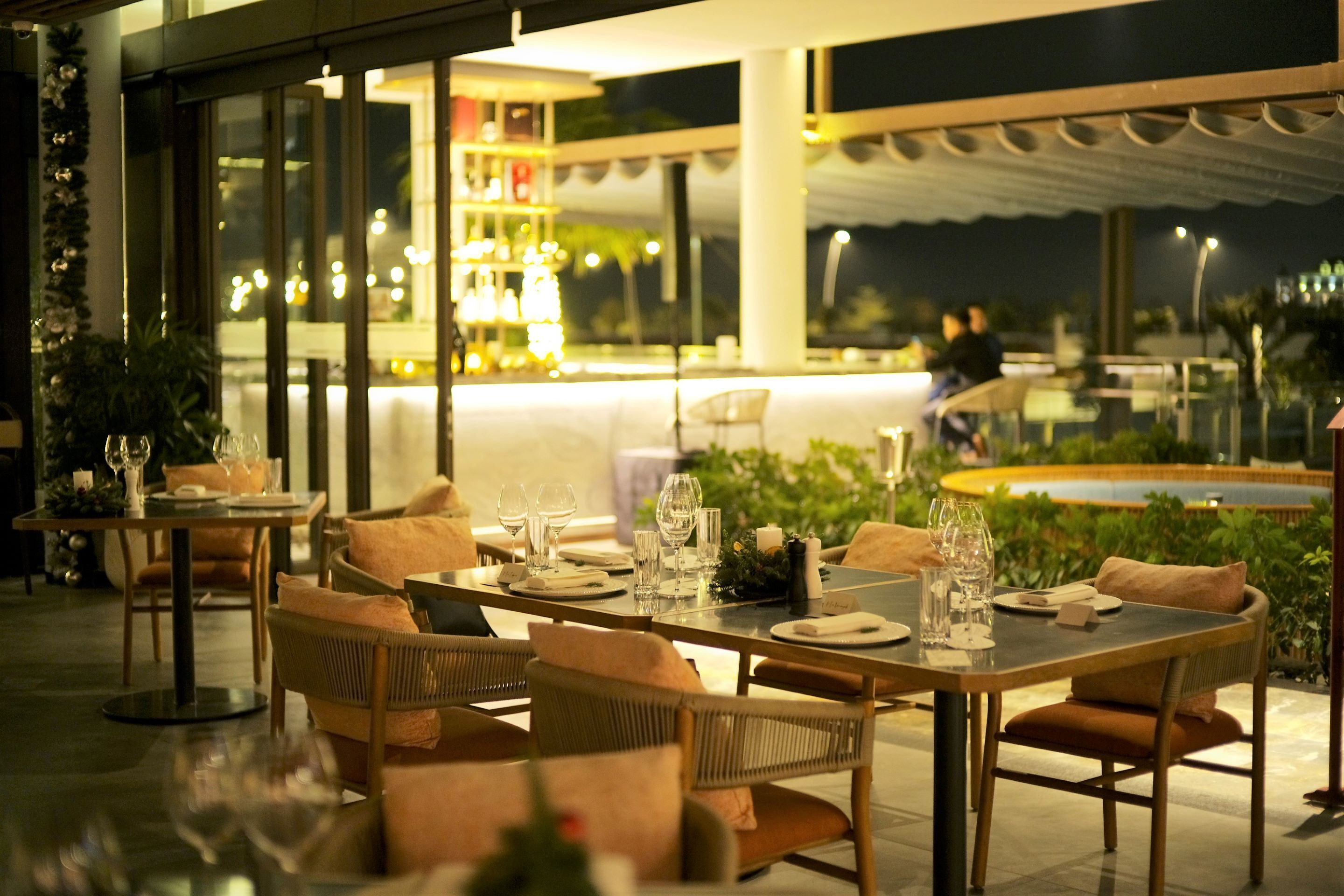 An outdoor dining area with tables set for two, surrounded by wicker chairs and cushions.