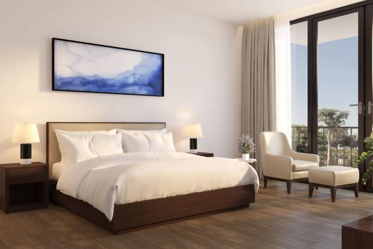 Habitación de hotel moderna con una cama grande, dos mesitas de noche con lámparas, una silla y un amplio ventanal con vistas.
