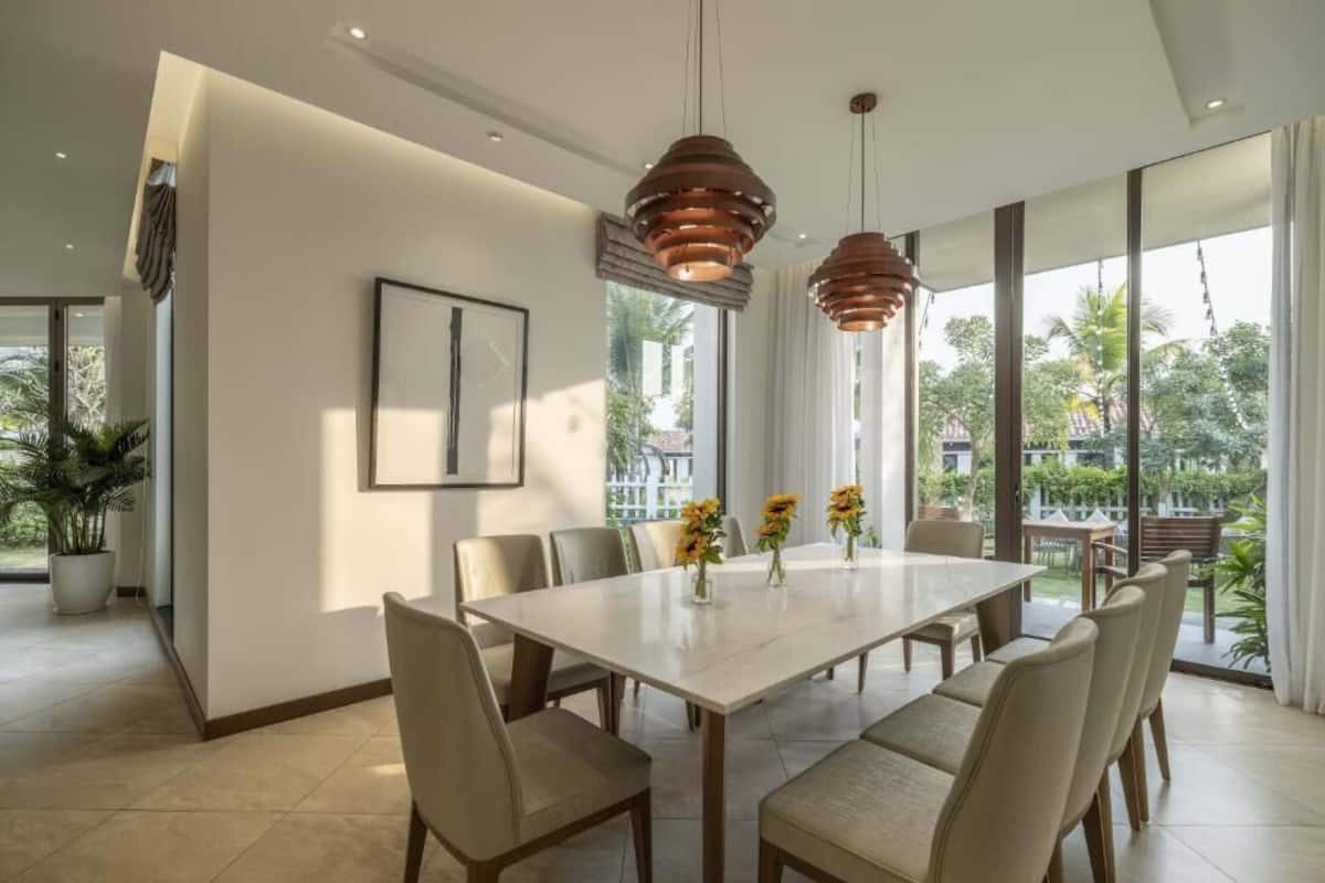 A modern dining area with a large table, chairs, pendant lights, and a view of the outdoors.