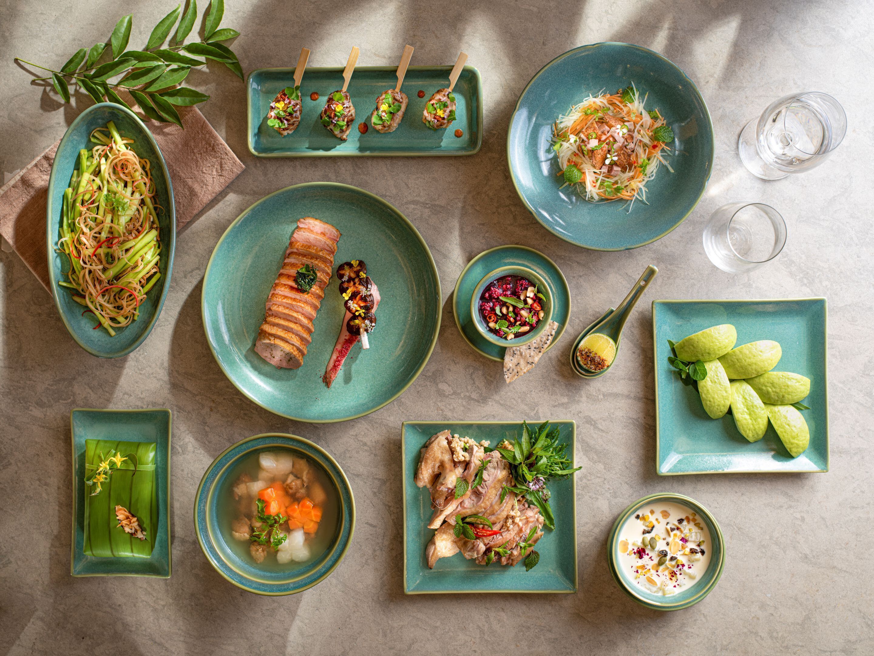 A variety of dishes on teal plates, including a rolled meat dish, a bowl of soup, and a salad with vegetables and nuts.