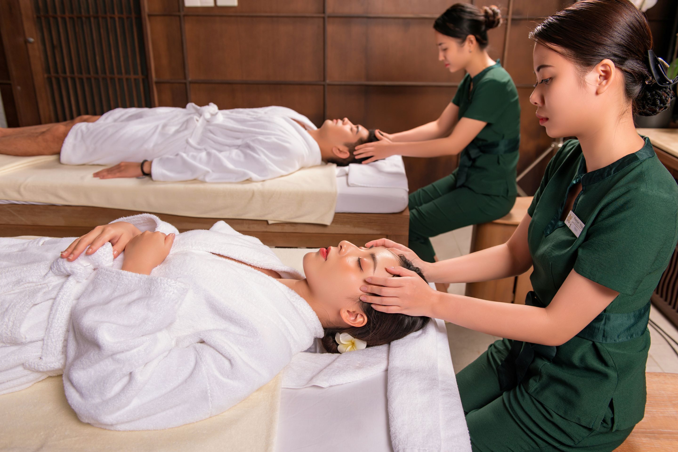 A spa setting with a massage table, a person receiving a head massage, and another person attending to a client.