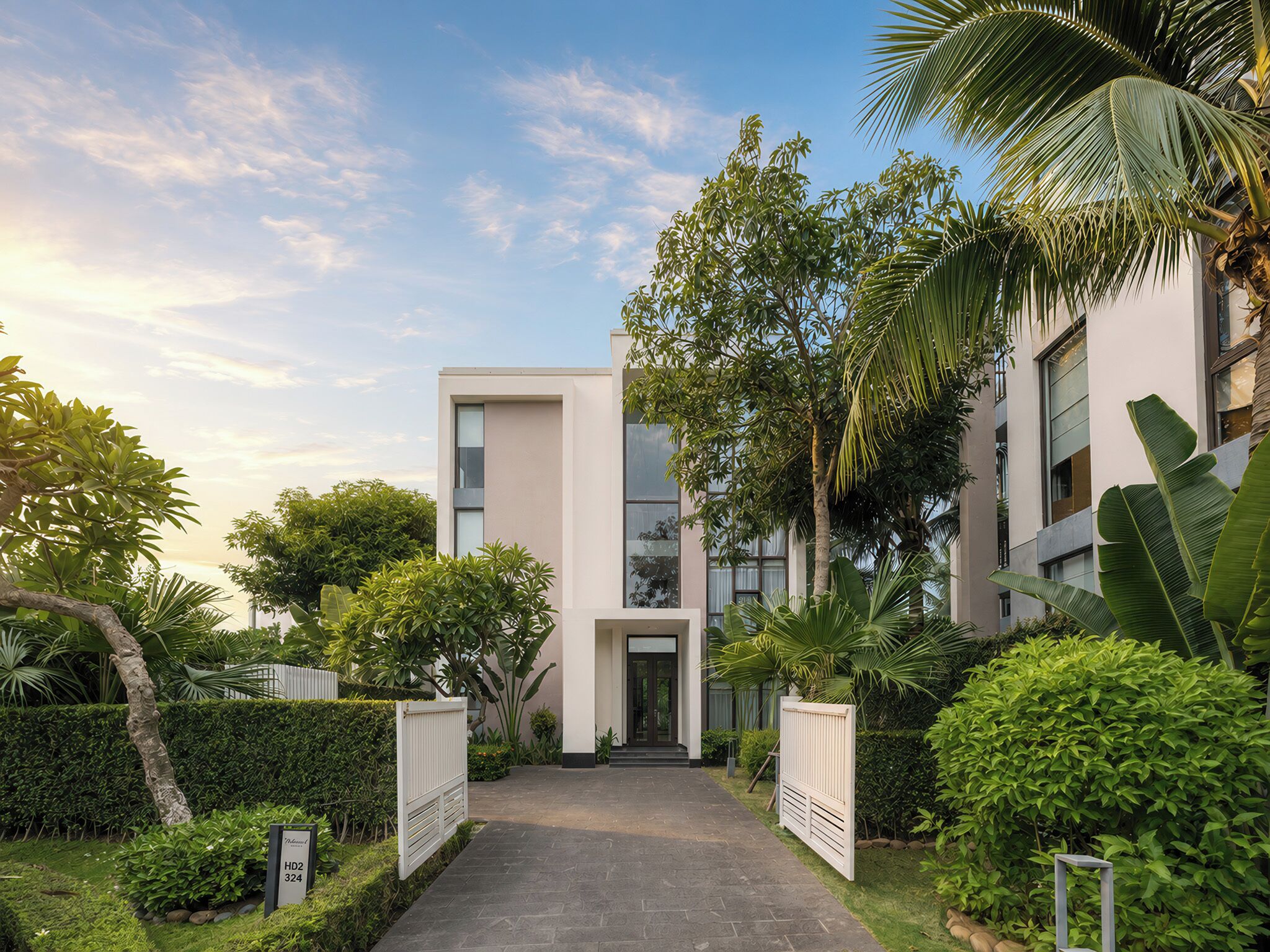 A modern building with a central entrance, surrounded by lush greenery and palm trees.