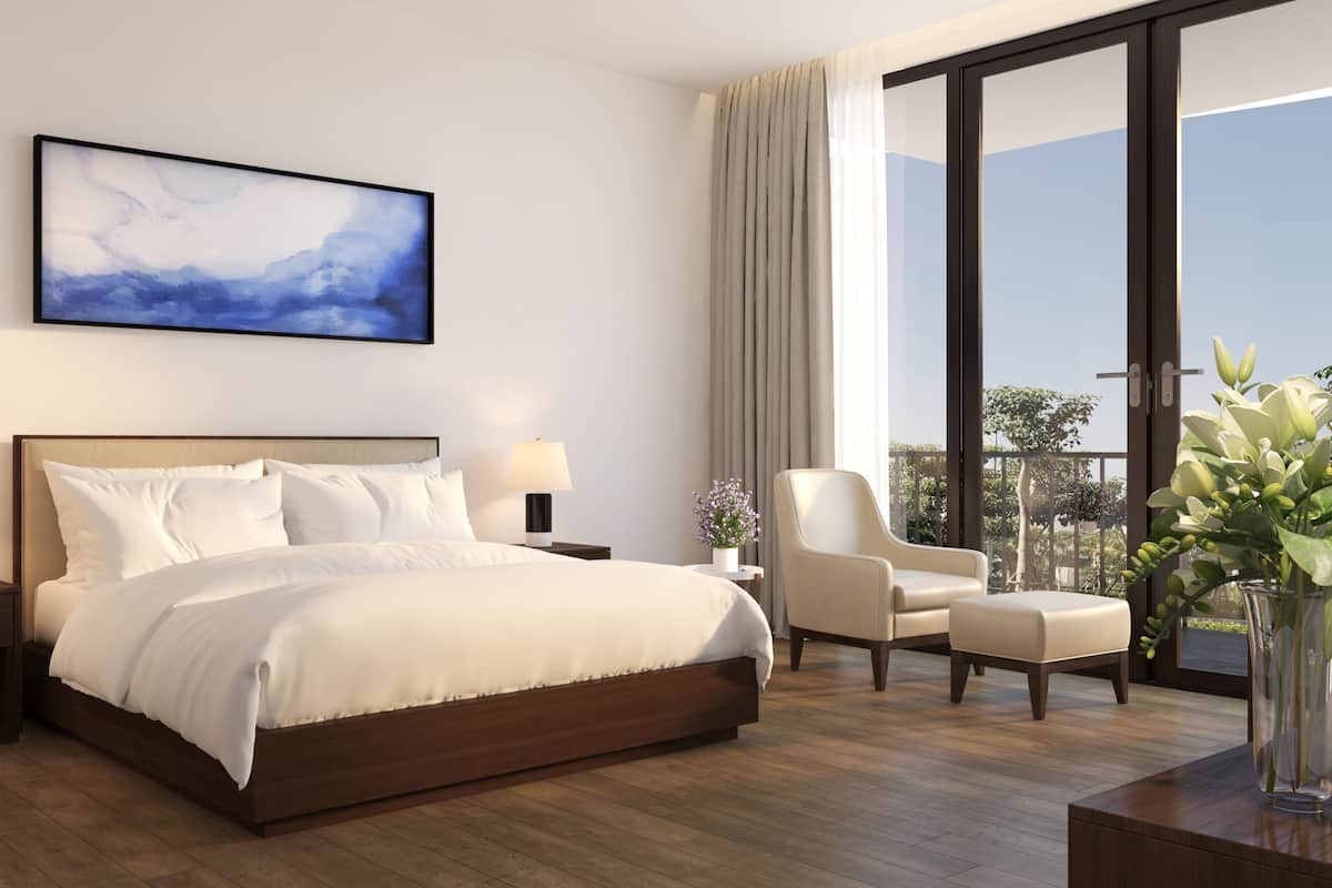 A modern hotel room with a large bed, two bedside tables with lamps, a chair, a desk, and a large window offering a view of the outdoors.