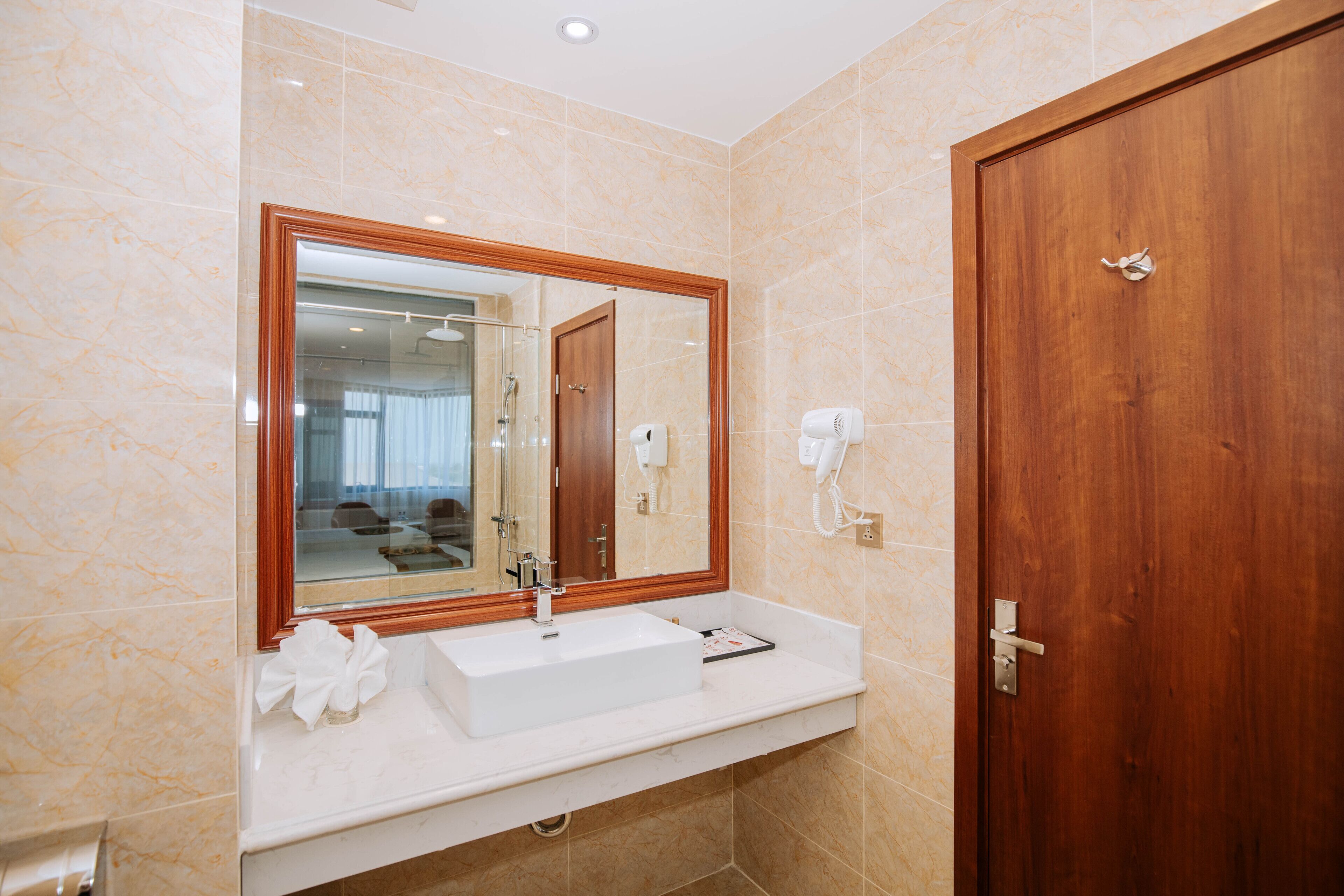Un baño con pared de mármol, puerta de madera, lavabo blanco y espejo con marco de madera.