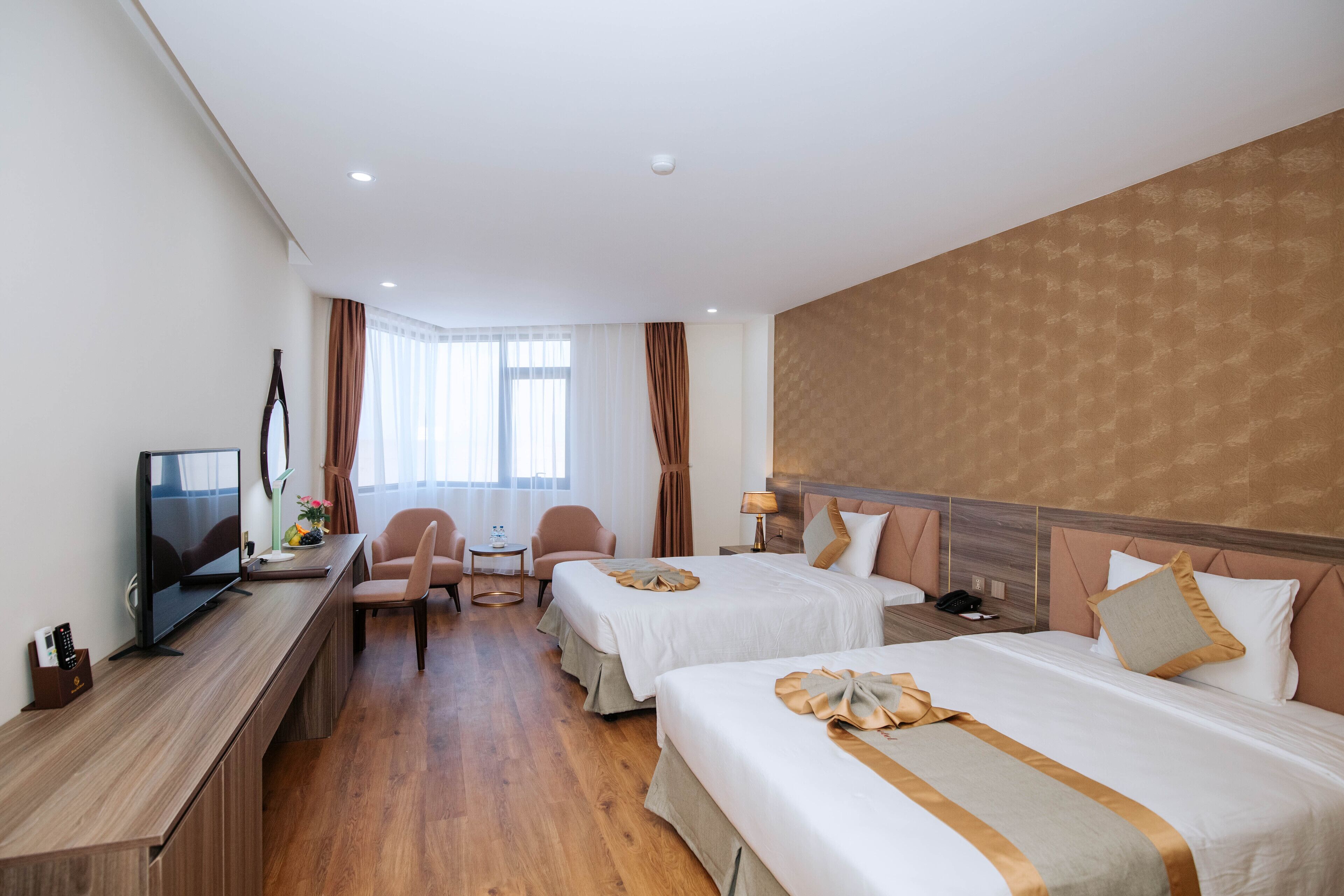 Une chambre d’hôtel avec deux lits, un bureau avec une télévision, une chaise et une petite table avec une lampe.