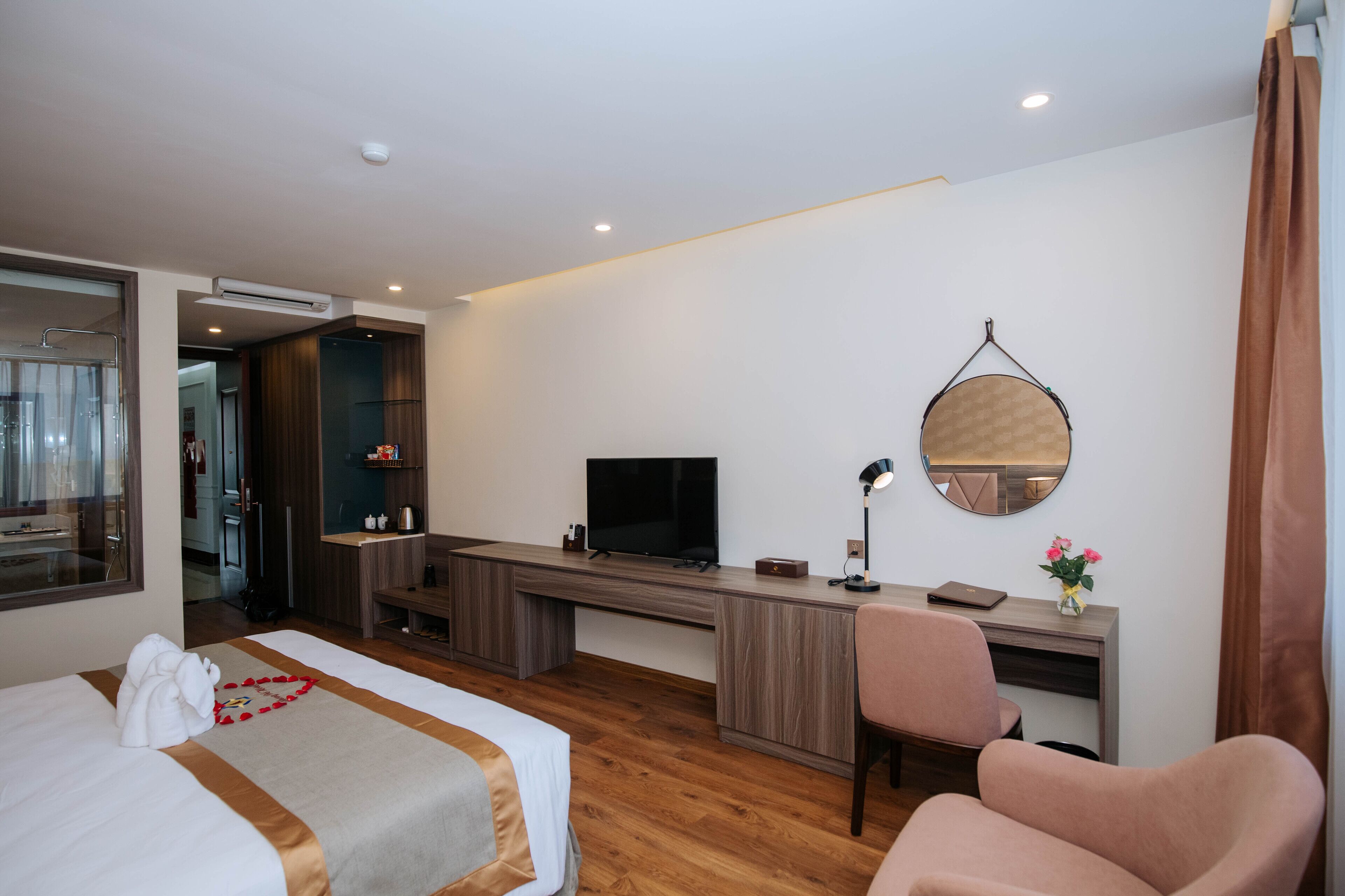 A hotel room with a bed, a desk, a chair, a TV, a mirror, and a bathroom visible through an open door.