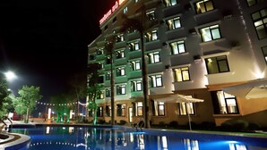 Un hotel con piscina, varios pisos y ventanas iluminadas.