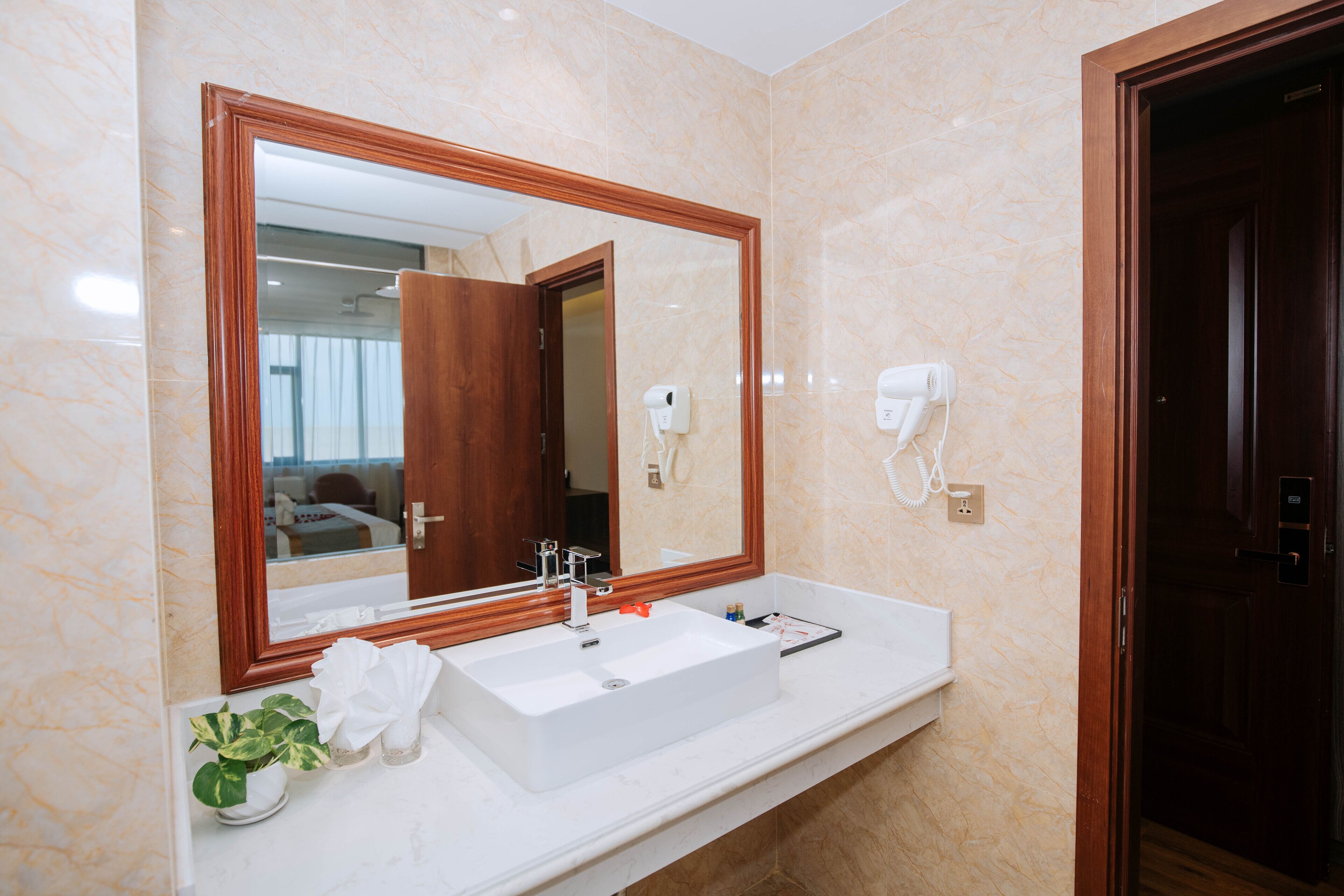 Un bagno con uno specchio grande, un lavandino bianco e un asciugacapelli montato a parete.
