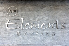 Un letrero con el texto "THE Elements @AMPANG" sobre una pared con textura.
