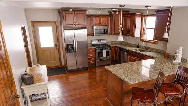 A kitchen with wooden cabinets, stainless steel appliances, granite countertops, and a dining area with two chairs. - Blocks to Downtown. Charming 3 Bed, Entire House (Stillwater)