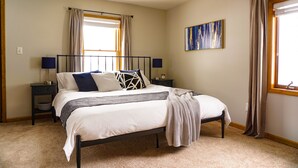 A bedroom with a bed, two bedside tables, a window with curtains, a painting on the wall, and a carpeted floor. - Blocks to Downtown. Charming 3 Bed, Entire House (Stillwater)