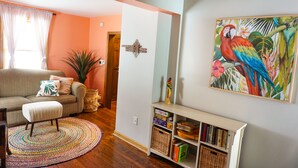 A living room with a sofa, a coffee table, a bookshelf, and a painting of a parrot. - Blocks to Downtown. Charming 3 Bed, Entire House (Stillwater)