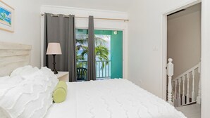 A bedroom with a bed, a nightstand, a lamp, a view of the outside, and a staircase. - Nautilus One – A Beachfront Condo on Seven Mile Beach - by Cayman Villas (West Bay)