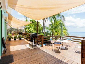 A wooden deck with outdoor furniture, a grill, and a view of the ocean.