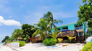 A beachside hotel with a pool, palm trees, and a clear blue sky. - Nautilus One – A Beachfront Condo on Seven Mile Beach - by Cayman Villas (West Bay)