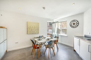 A modern kitchen with a dining table, chairs, a clock, and a window.