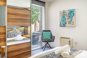 A hotel room with a bed, a chair, a radiator, and a painting on the wall.