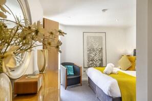 Habitació d'hotel moderna amb un llit, una cadira, un mirall gran i una obra d'art penjada a la paret.