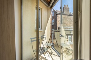 A glass door leading to a balcony with a metal chair, a window, and a brick building in the background. - 12 Stonegate Court - sleeps 4 guests in 2 bedrooms (York)