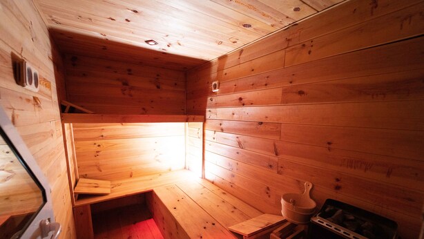Interior de una cabaña de madera con un banco, una mesita y una estufa.