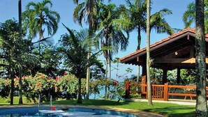 A pool area with a wooden deck, surrounded by palm trees and tropical plants.