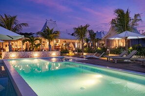 A swimming pool with lounge chairs and umbrellas, surrounded by palm trees and a stone wall. - Paus Putih Hotel (Lembongan Island)