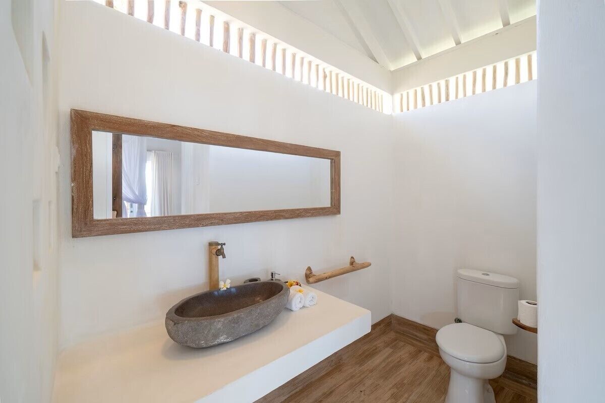 A bathroom with a stone sink, wooden shelf, and a white toilet.