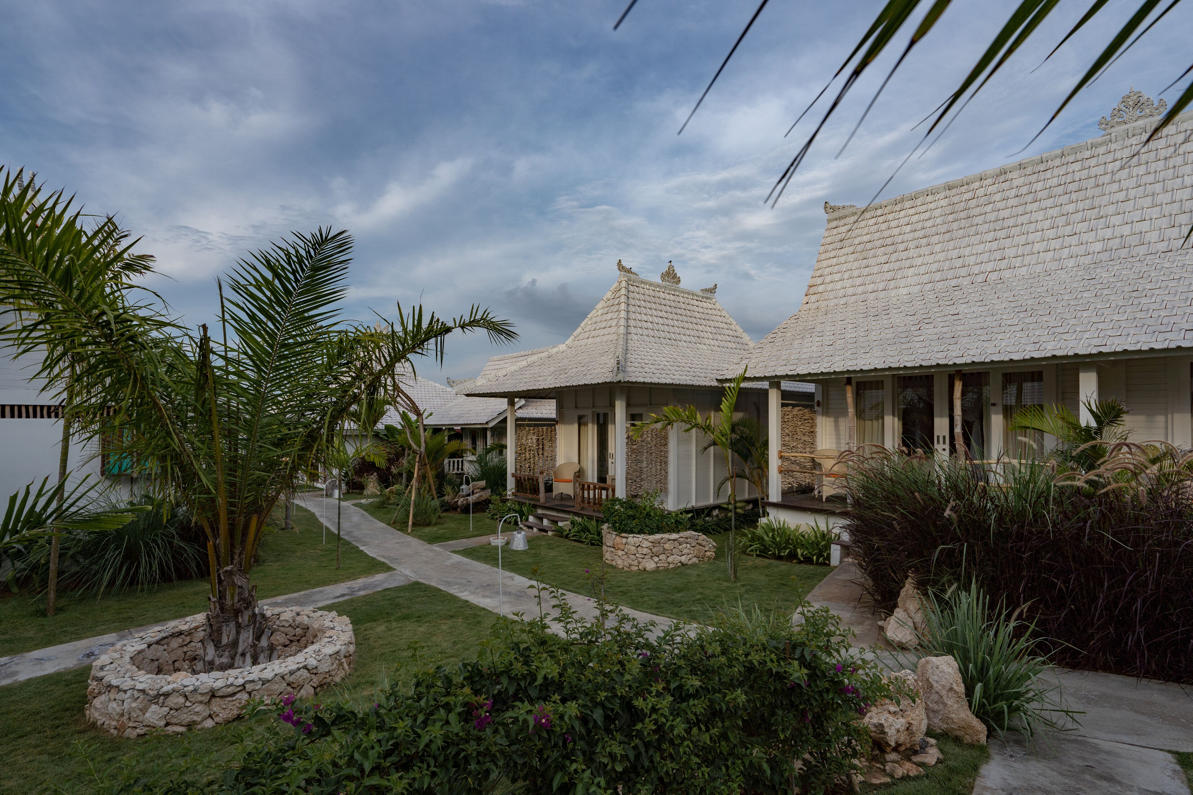 A traditional house with a tiled roof, surrounded by a well-maintained garden with palm trees and a stone pathway.