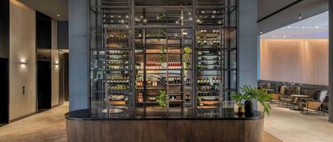 A modern bar area with a central counter, shelves with bottles, and seating in the background.