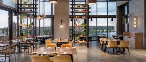 Un restaurante moderno con techos altos, ventanas amplias y diversas opciones de asientos.