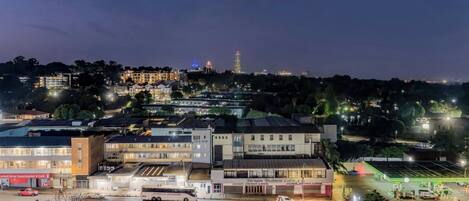 Une vue nocturne d’une zone commerciale avec des immeubles, un autobus et un parking.