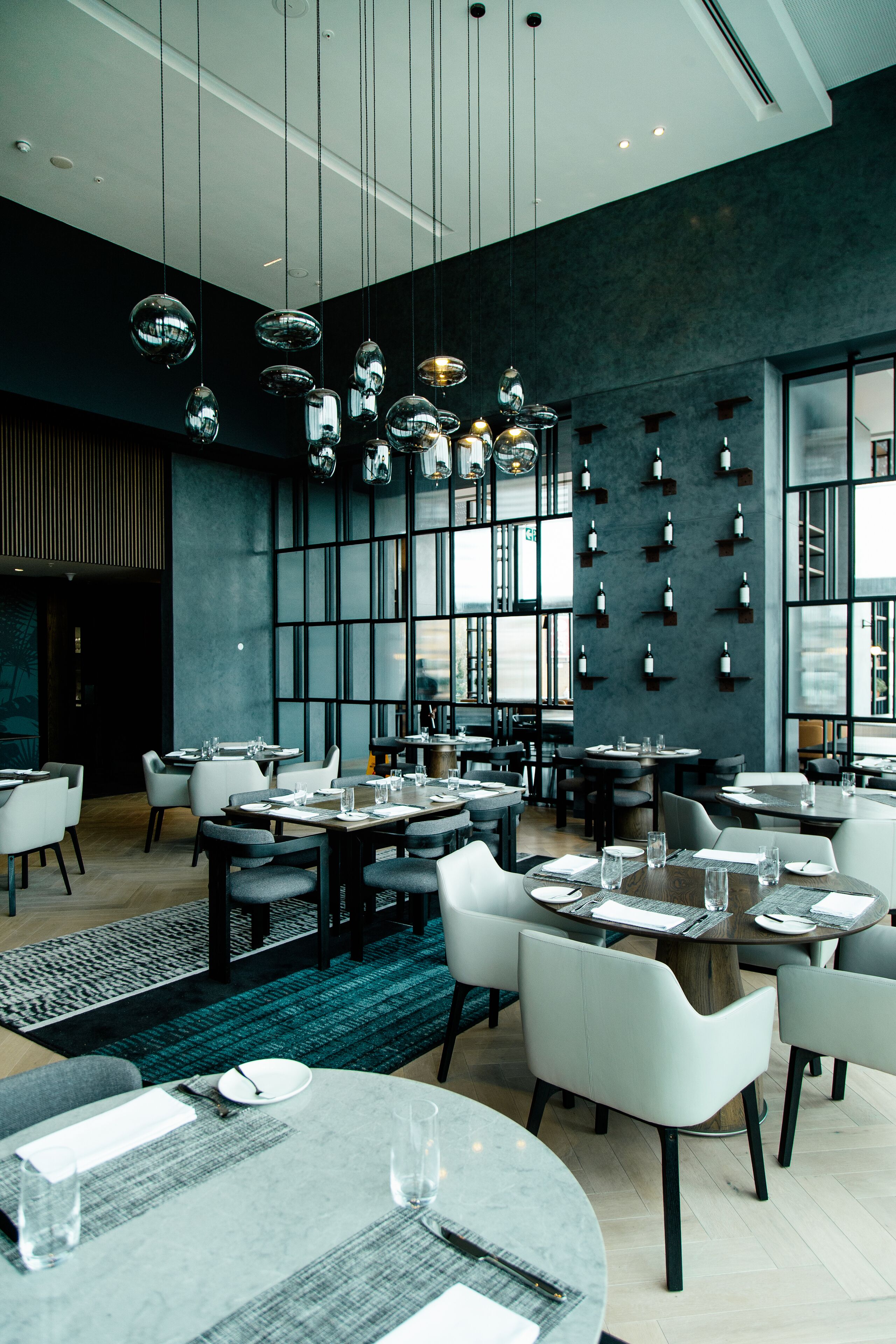 Un restaurant moderne avec des tables rondes, des chaises blanches et des luminaires sphériques suspendus au plafond.