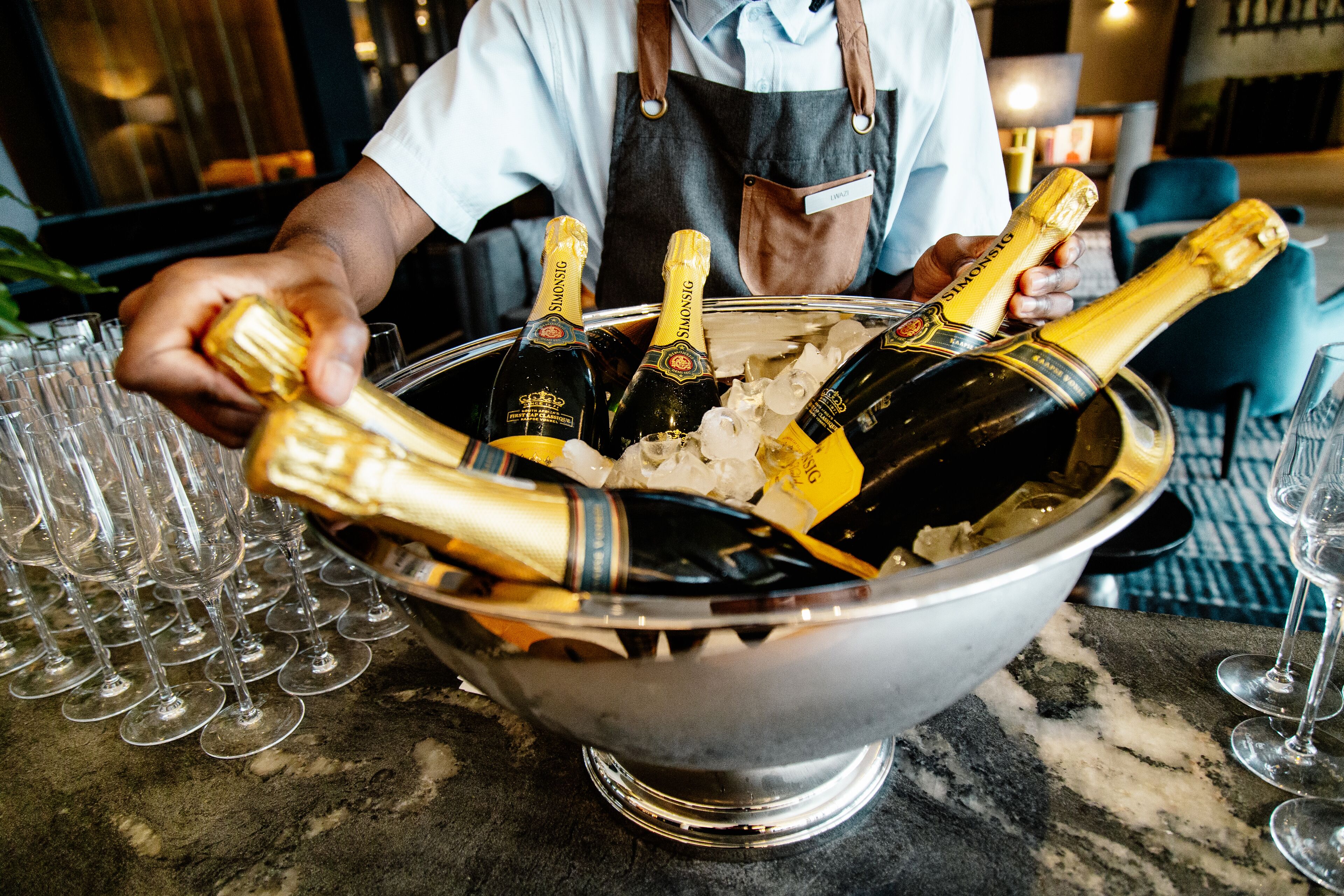 A person pouring champagne into a large metal bucket filled with ice and champagne bottles.