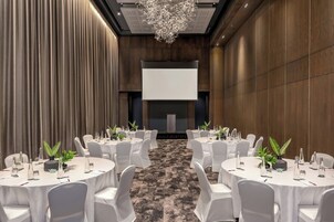 A conference room with round tables, white chairs, and a projector screen at the front.