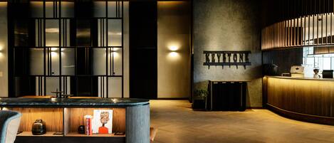 A modern hotel lobby with a reception desk, a bar area, and a seating area with a coffee machine.