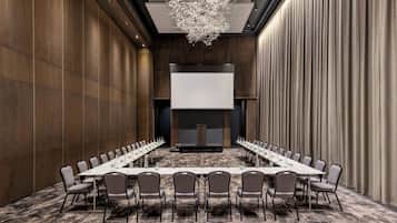 A conference room with a long table, chairs, a projector screen, and a chandelier.