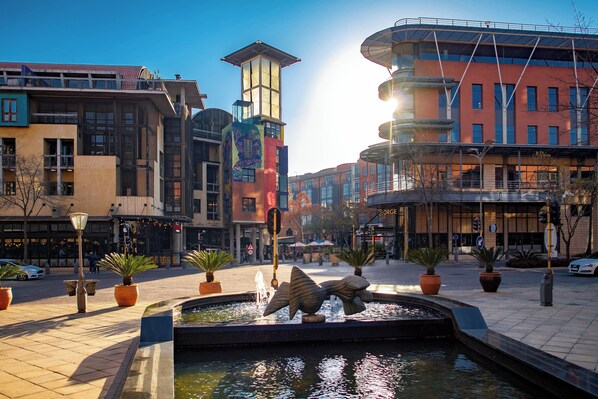A public square with a fountain, potted plants, and modern buildings.