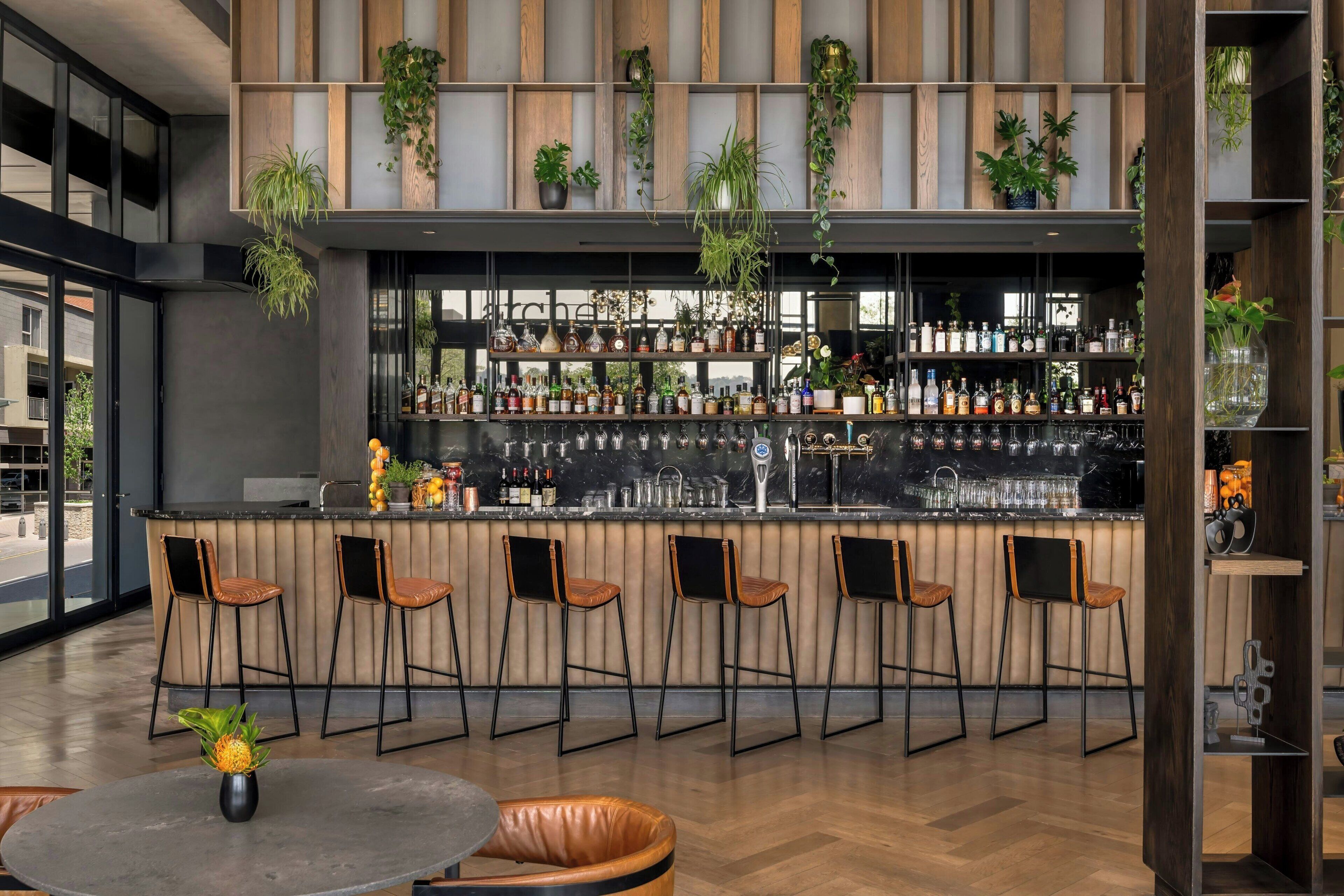 A modern bar area with a long counter, multiple bar stools, and a variety of bottles and glasses.