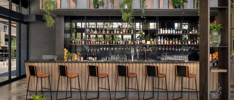 A modern bar area with a long counter, multiple bar stools, and a variety of bottles and glasses.