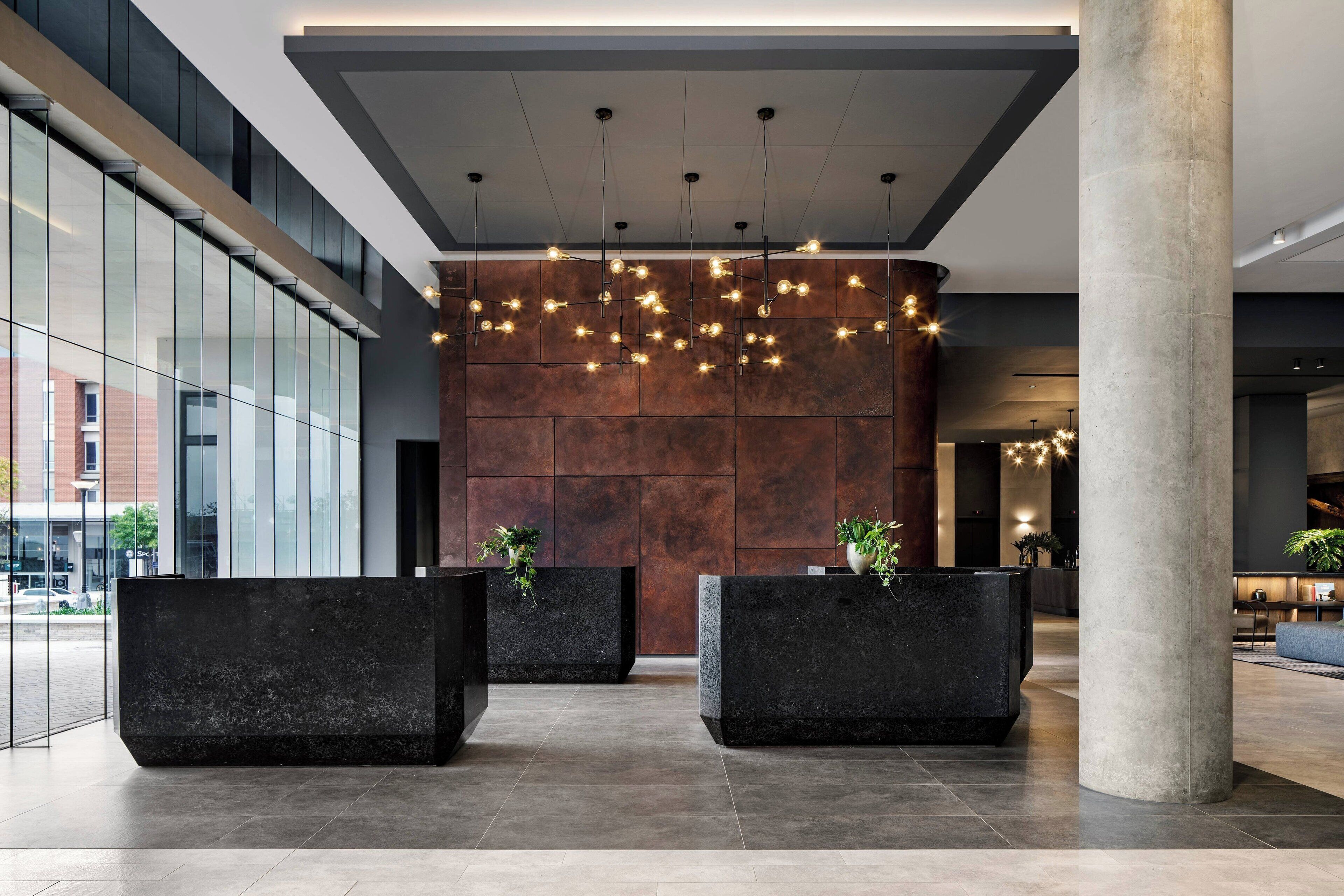 Un vestíbulo moderno con amplias recepciones de color negro, una pared curva con luces colgantes y una gran columna.