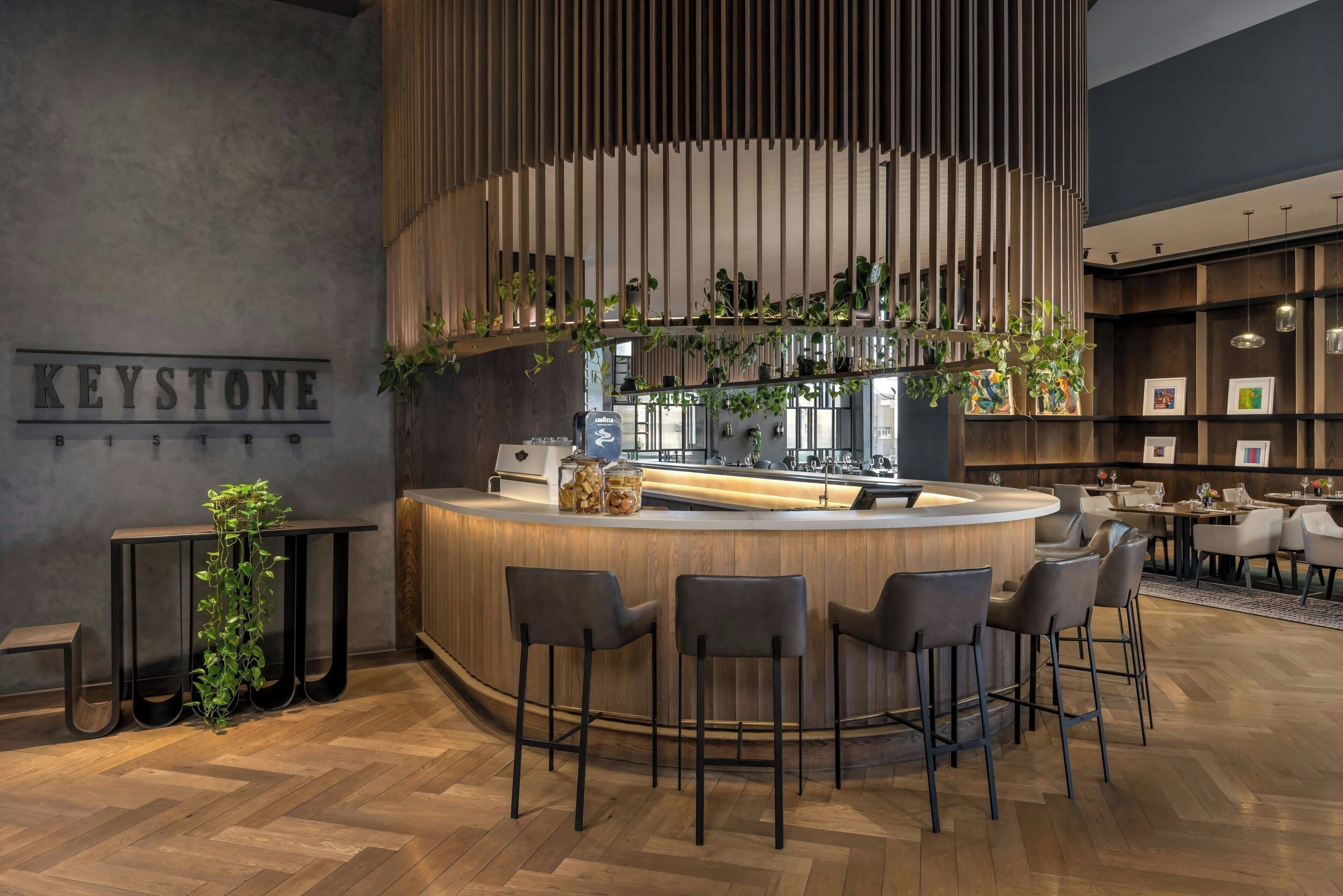 Een moderne bar met een houten toonbank, barstoelen en een bord waarop 'KEYSTONE BISTRO' staat.