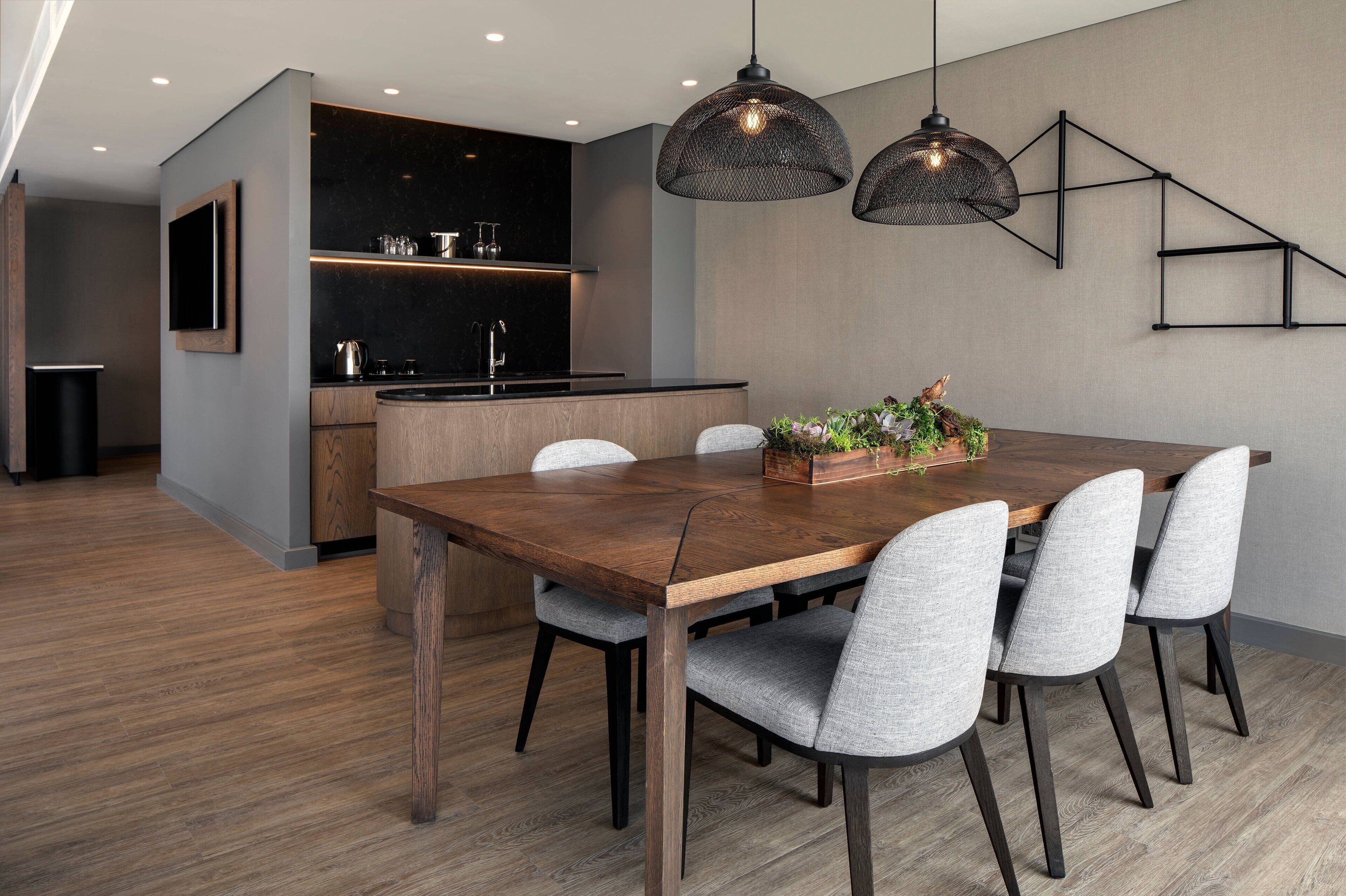 A modern kitchen with dark countertops, a wooden dining table, and grey upholstered chairs.