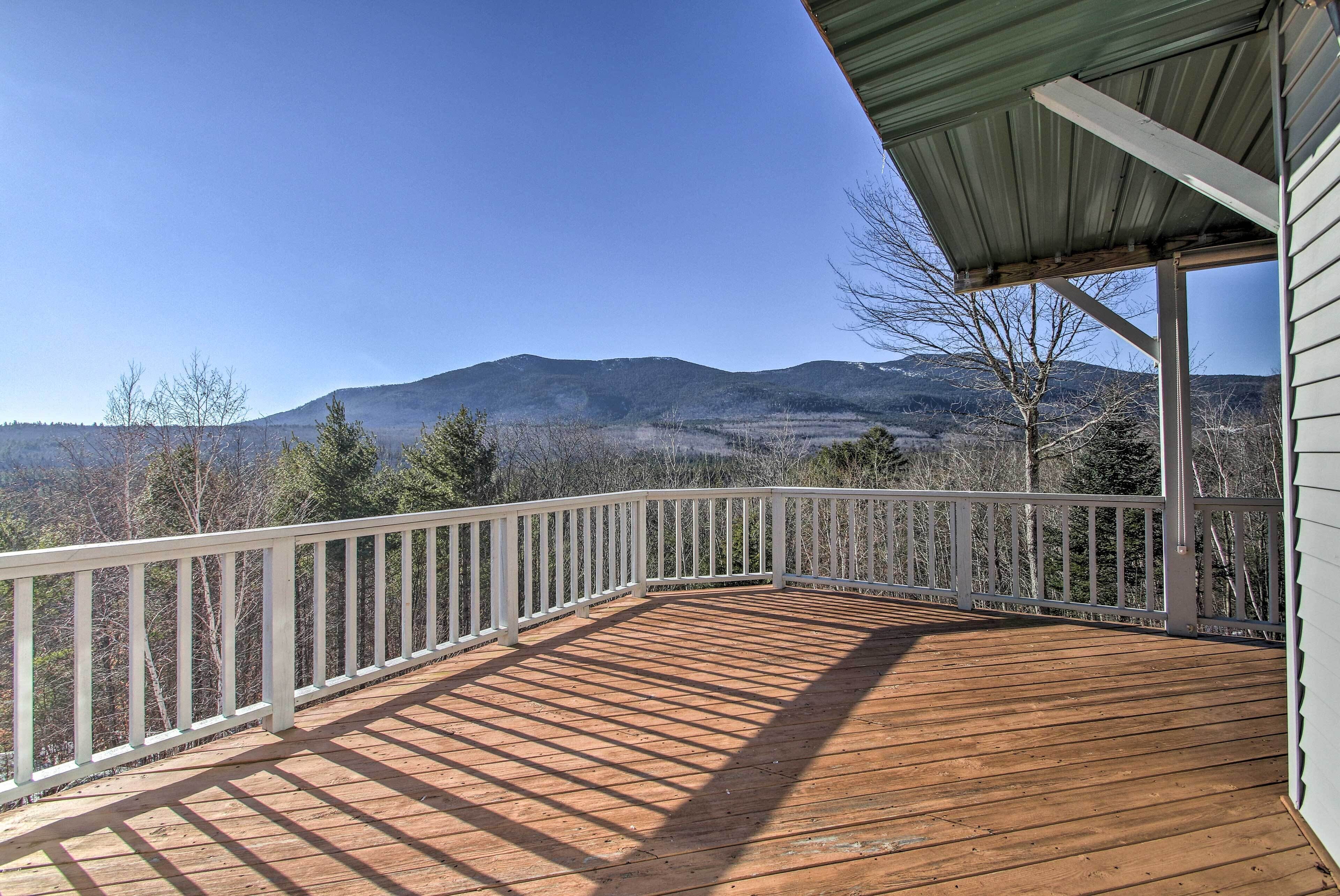 A wooden deck with a white railing, overlooking a mountainous landscape.