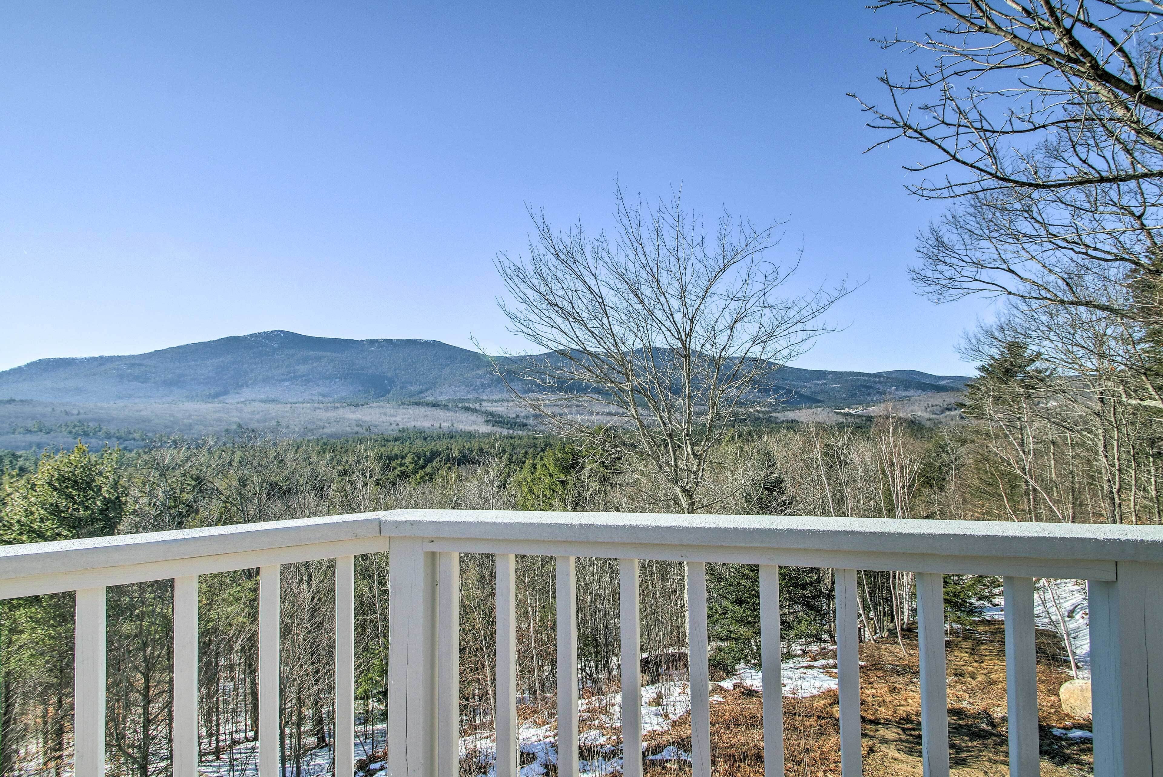 A view from a white balcony overlooking a forested landscape with mountains in the distance.