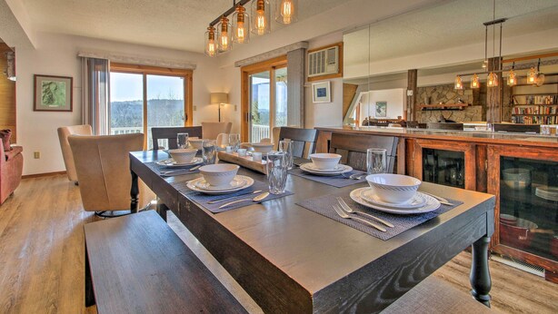 A dining area with a long wooden table set for four, a bench, and a kitchen area with a stone wall and bookshelves. - Hot Tub & Moat Mtn Views: North Conway Townhouse (North Conway)