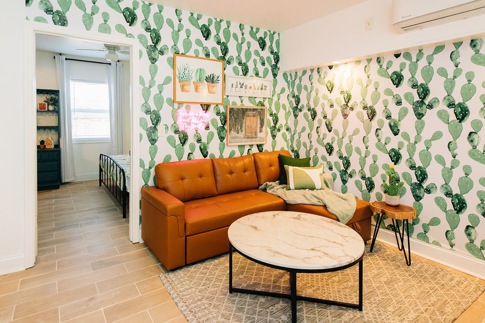 Una sala de estar con un sofá marrón, una mesa de centro redonda y un papel tapiz con motivos de cactus.