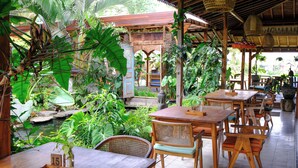 Un restaurant avec des tables et des chaises en bois, entouré d’une végétation luxuriante et d’un petit étang.