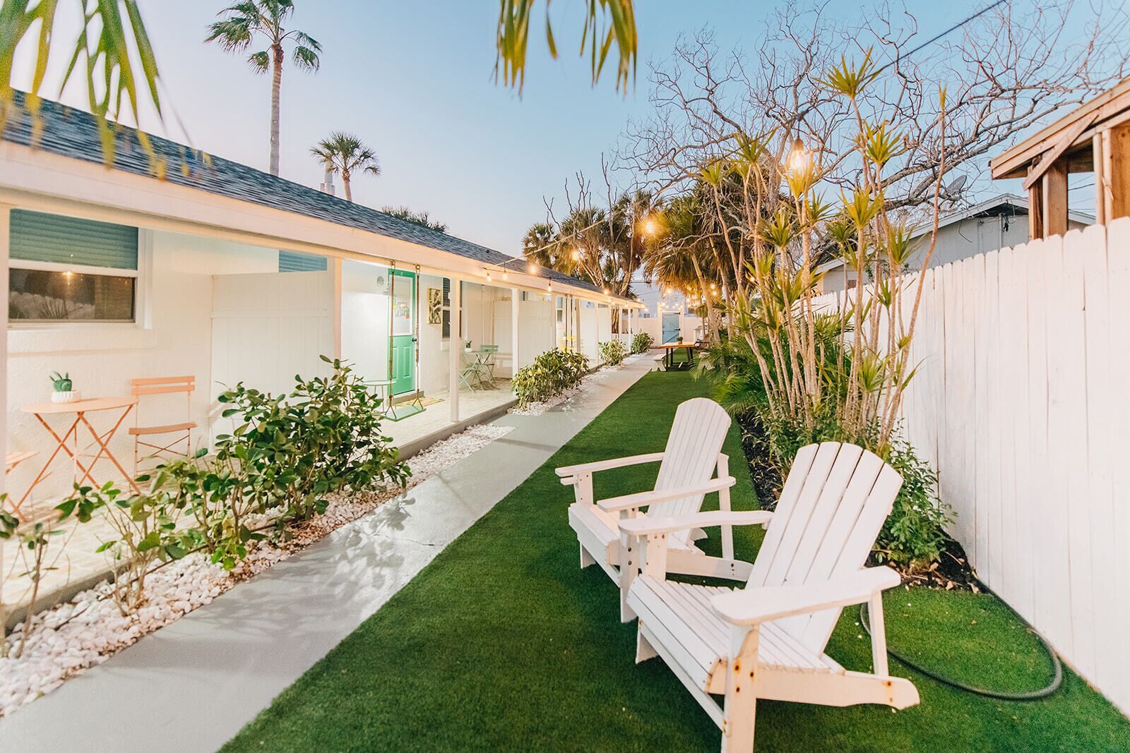 A row of white cabins with a paved walkway and green lawn, each with a small table and chairs.