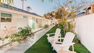 A row of white cabins with a paved walkway and green lawn, each with a small table and chairs.