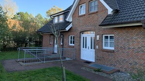 A two-story brick house with a gabled roof, a front door, and a small porch. - Apartment oasis in Dünenhof (St. Peter-Ording)